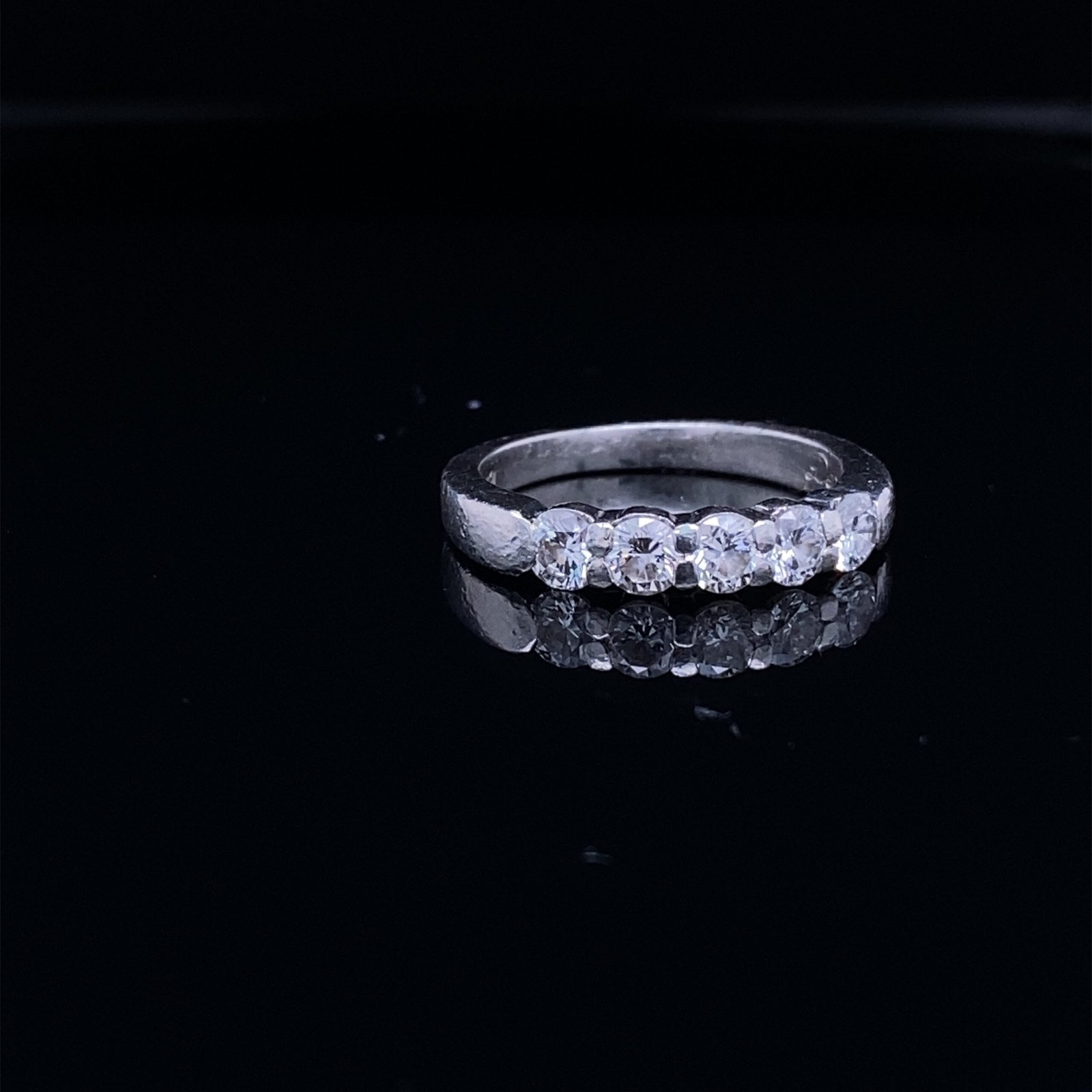 Silver diamond ring on black reflective surface